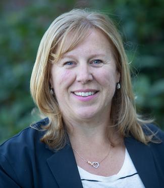 Smiling woman wearing a blue blazer, white shirt and necklace