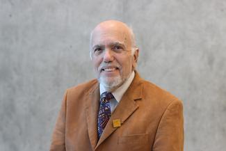 Nate Bello smiling, wearing a warm brown suit in an airy modern room